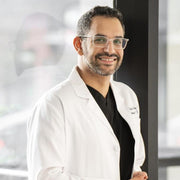A man in a white lab coat, wearing glasses and smiling, suggestive of a healthcare professional, relevant to nutritional supplement context.
